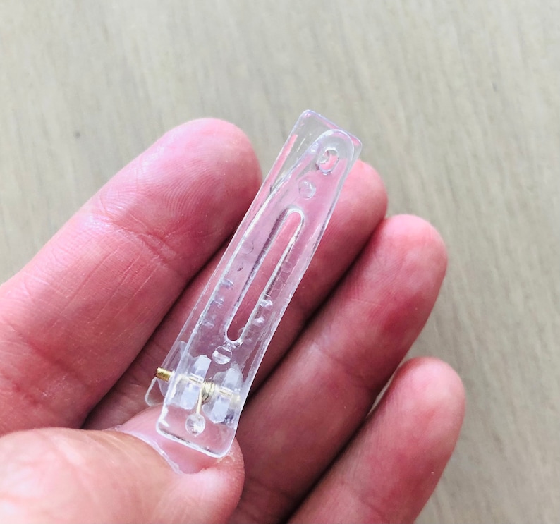 May include: A clear plastic hair clip with a metal spring. The clip is designed to hold hair in place.