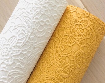 May include: Two rolls of lace fabric, one white and one yellow. The lace has a delicate floral pattern.