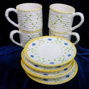 May include: A set of two ceramic mugs and four matching saucers featuring a white basket-weave texture, yellow rope-style rims, and a hand-painted pattern of small green leaf clusters and blue diamond accents on a white background.