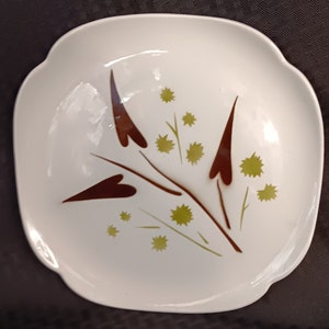 May include: White square serving dish with a brown and green floral design. The design features stylized leaves and flowers.