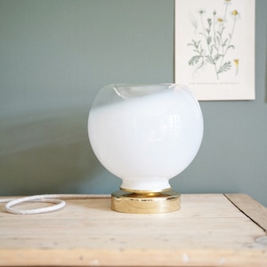 May include: A white glass globe table lamp with a gold metal base. The lamp is sitting on a wooden surface.