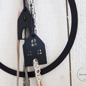Puede incluir: Adornos de madera negra en forma de casa con ventanas recortadas que cuelgan de un aro de metal negro con cuerda blanca y marr&oacute;n. El texto "Decofieber" es visible en la esquina inferior derecha.