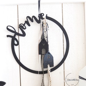 Puede incluir: Decoraci&oacute;n para el hogar de metal negro con una corona y la palabra "home" en una fuente de escritura. La corona tiene dos adornos negros en forma de casa colgando de ella.