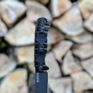May include: Black folding knife with a textured black handle and a black blade. The handle has a textured grip and the blade is partially visible.