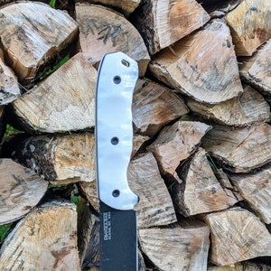 May include: A white handled knife with a black blade, leaning against a stack of firewood.