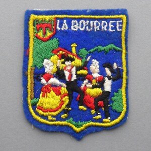 Peut inclure: Patch brodé avec un fond bleu et une bordure jaune. Le patch présente un blason avec un motif rouge, blanc et vert et le texte "LA BOURREE". L'image principale montre un groupe de personnes dansant en costumes traditionnels.