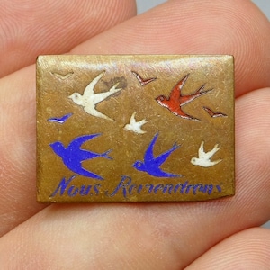 Puede incluir: Un pin de metal dorado con un diseño de esmalte azul y blanco de pájaros volando. El pin tiene el texto "Nous Retournons" en esmalte negro.