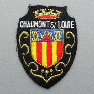 May include: Embroidered patch with a black background and gold trim. The patch features a shield with a red, yellow, and blue design and the text "CHAUMONTS/LOIRE" in white.