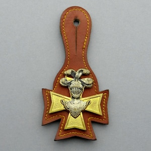 Peut inclure: Une sangle en cuir marron avec une croix en métal doré et argenté et un motif de casque de chevalier.