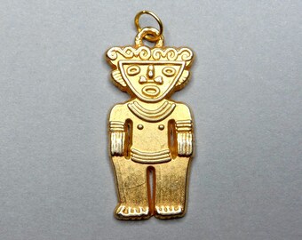 Puede incluir: Pendiente de oro con una figura humana estilizada con una cara y patrones geométricos. El pendiente tiene un bucle en la parte superior para sujetar una cadena.