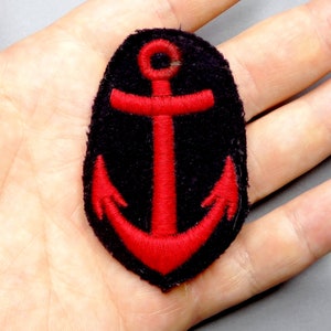 Op de afbeelding: Een rode geborduurde anker op een zwarte vilt patch.
