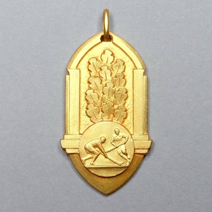 Puede incluir: Una medalla de color dorado con un diseño en relieve de dos figuras jugando al hockey sobre hierba. La medalla tiene forma de arco con una corona de laurel en la parte superior.