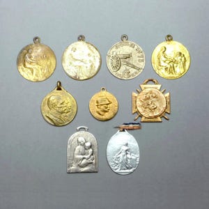 May include: A collection of nine vintage gold and silver medals with various designs, including a soldier, a cannon, and a religious figure.