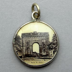 Op de afbeelding: Een zilveren bedel met een zwart-witfoto van een boog met de tekst "Châlons s. Marne Porte St. Croix."