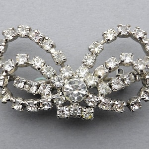Op de afbeelding: Een zilverkleurige broche met een strikdesign gemaakt van heldere strass.