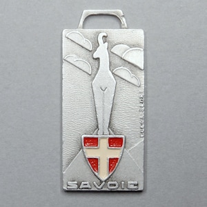 May include: A silver metal keychain with a white ibex silhouette and a red and white cross on a shield. The keychain says "SAVOIE" at the bottom.