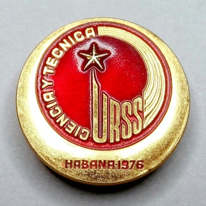Puede incluir: Un pin redondo dorado con un centro rojo que presenta el texto dorado "CIENCIA Y TECNICA" y "URSS". Una estrella dorada en la parte superior. El texto "HABANA 1976" está en la parte inferior.