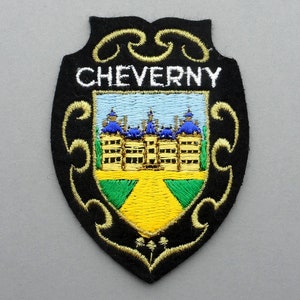 May include: A black embroidered patch with a gold border and the word "CHEVERNY" in white. The patch features a colorful embroidered image of a castle with blue roofs and yellow walls.