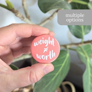 May include: A pink button with the text "weight != worth" in white lettering.