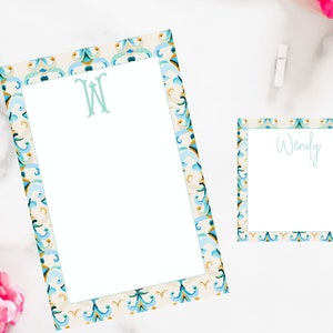 May include: Two white stationery notepads with a blue and gold patterned border. The larger notepad has a green monogram "W" on the top. The smaller notepad has the name "Wendy" written on the top.