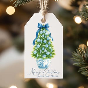 May include: A white rectangular gift tag with a jute string, featuring a watercolor illustration of a green Christmas tree in a blue and white patterned pot, decorated with blue ornaments and a blue bow, with the text Merry Christmas JOHN & SARA MILLER.