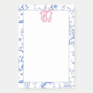May include: White notepad with a blue and white floral border. The notepad has a pink monogram in the centre.