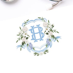 May include: A white card with a blue and white floral monogram featuring the letter "H" in a crest. The monogram is surrounded by white flowers and blue ribbon.