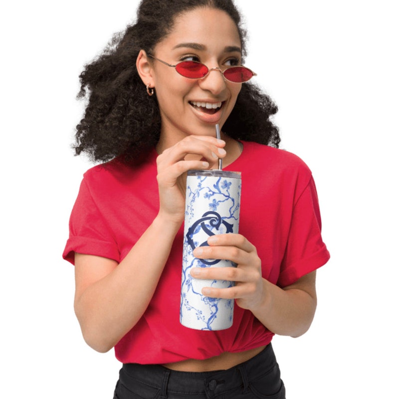 May include: A white stainless steel tumbler with a blue and white floral design and a blue monogram. The tumbler has a lid and a straw.