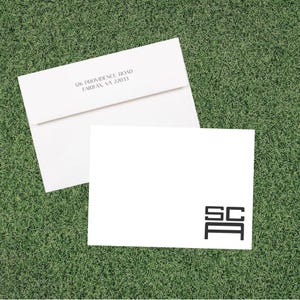 May include: Two white stationery items on a green surface. One is an envelope with the address "126 Providence Road Fairfax, VA 22033" printed in black. The other is a blank card with the initials "SCA" in a black, geometric design.