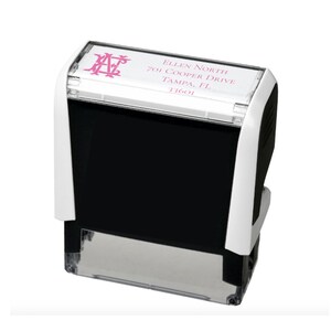 K&ouml;nnte beinhalten: Ein selbstf&auml;rbender Adressstempel mit wei&szlig;em und schwarzem Geh&auml;use. Die Oberseite zeigt ein rosa Monogramm und Adressdetails: Ellen North, 701 Cooper Drive, Tampa, FL 33601. Der Stempel ist f&uuml;r einen klaren und effizienten Abdruck konzipiert.