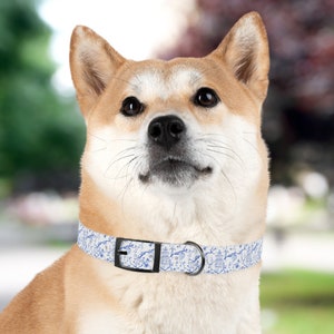 Op de afbeelding: Een Shiba Inu hond die een wit en blauw gepatroneerd hondenhalsband draagt met een zwarte gesp. De halsband heeft een blauw en wit bloemenpatroon met een pagodepatroon.