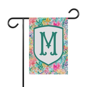 Peut inclure: Un drapeau de jardin floral color&eacute; avec un bouclier blanc sur lequel est inscrit une lettre "M" verte au centre. Le drapeau est con&ccedil;u pour une utilisation en ext&eacute;rieur et est parfait pour ajouter une touche de personnalit&eacute; &agrave; votre jardin.