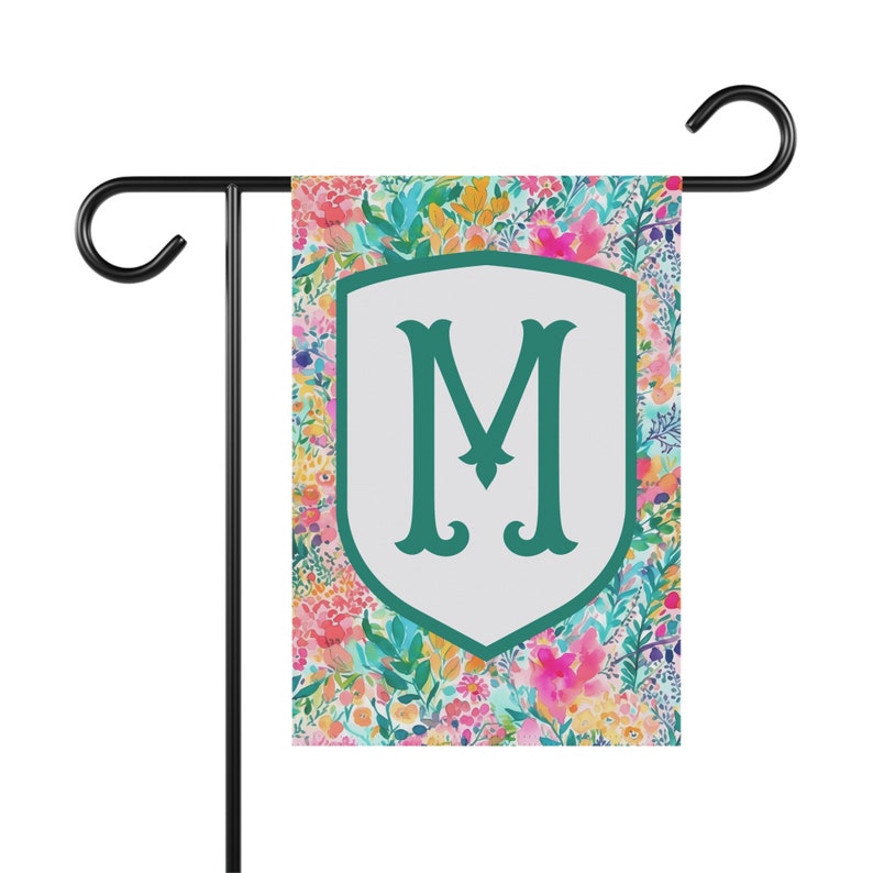Peut inclure: Un drapeau de jardin floral color&eacute; avec un bouclier blanc sur lequel est inscrit une lettre "M" verte au centre. Le drapeau est con&ccedil;u pour une utilisation en ext&eacute;rieur et est parfait pour ajouter une touche de personnalit&eacute; &agrave; votre jardin.