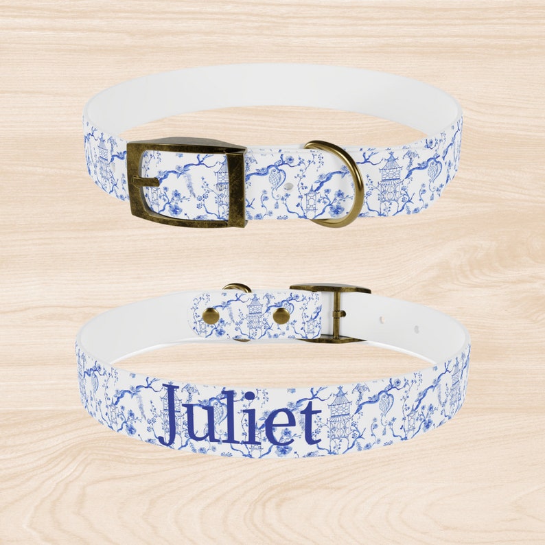 Op de afbeelding: Witte hondenhalsband met een blauw en wit bloemenpatroon en gouden beslag. De halsband is gepersonaliseerd met de naam "Juliet".