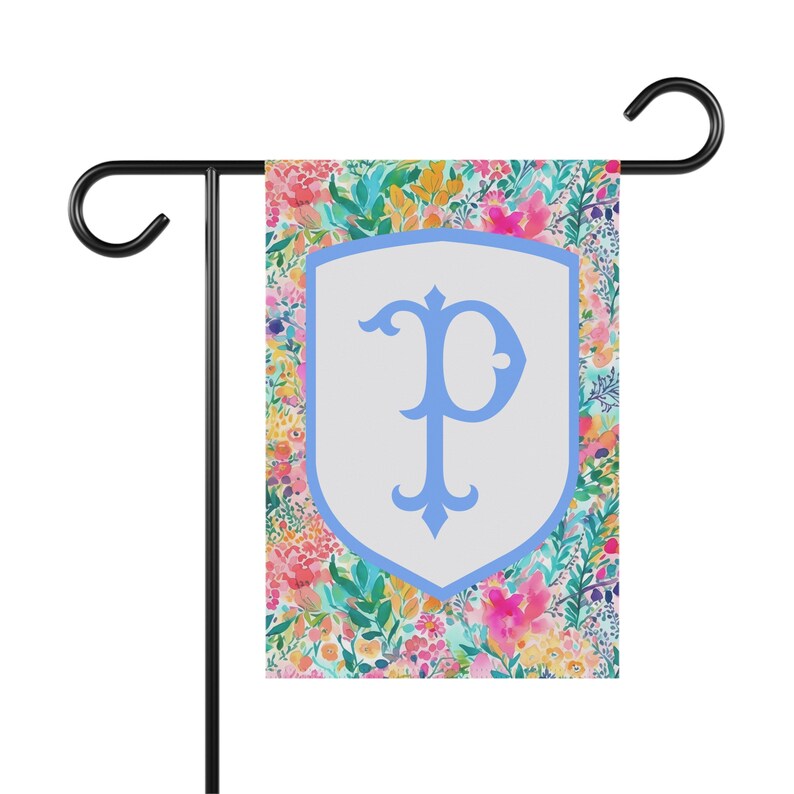 Peut inclure: Un drapeau de jardin avec un motif floral dans des tons de rose, jaune et vert. Un bouclier blanc avec une lettre "P" bleue est au centre du drapeau.
