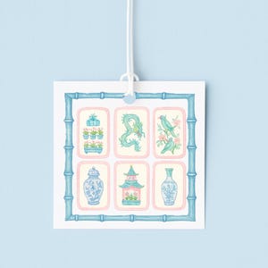 May include: A square card with a blue bamboo-style border and six rectangular illustrations. The illustrations feature Asian-inspired designs in blue and pink, including a dragon, birds, and vases. The card is suspended by a white string against a light blue background.