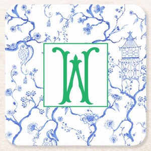 May include: Square coaster with a white background and a blue floral Chinoiserie design. A green letter "W" is centered within a green square. The coaster features a pagoda and floral branches.