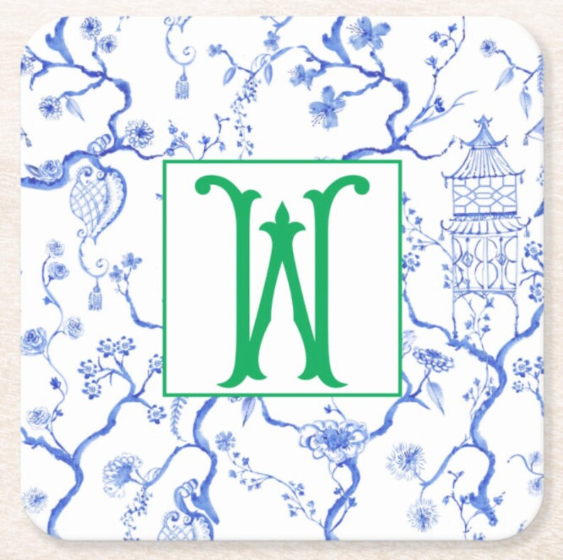 May include: Square coaster with a white background and a blue floral Chinoiserie design. A green letter "W" is centered within a green square. The coaster features a pagoda and floral branches.