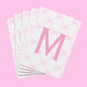 May include: A stack of white cards with a pink bow pattern and the letter "M" printed in pink.