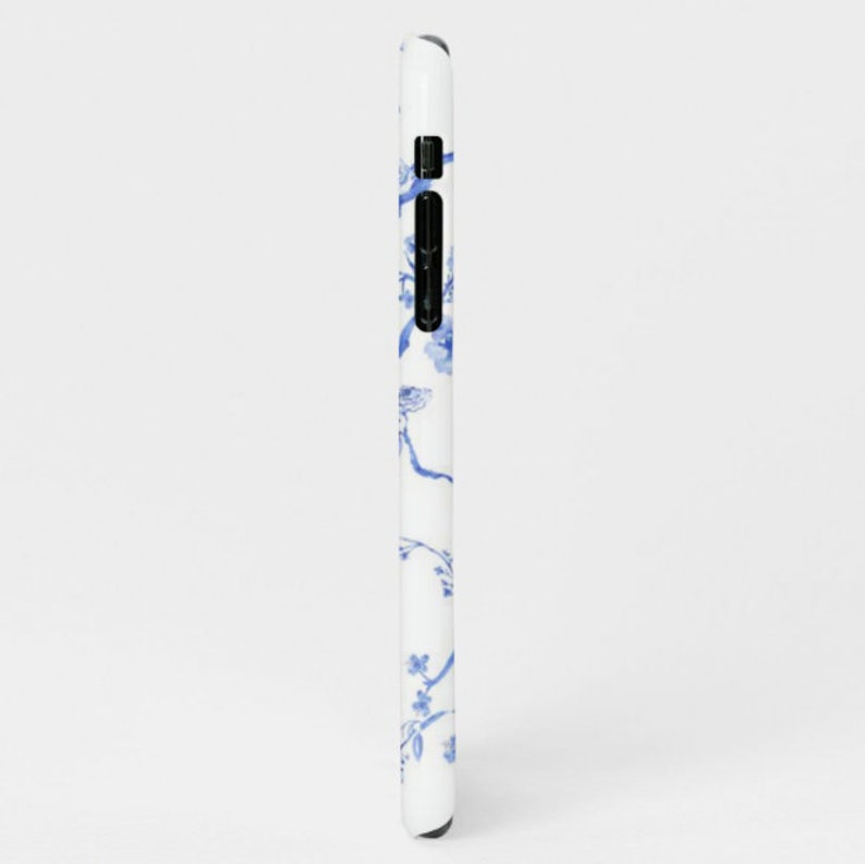 May include: A white phone case with a blue floral pattern. The pattern features delicate branches with small blue flowers.