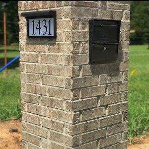 May include: A brick pillar with a black mailbox and address plaque. The address plaque displays the number "1431" in black against a white background. The mailbox is a standard design with a locking door.