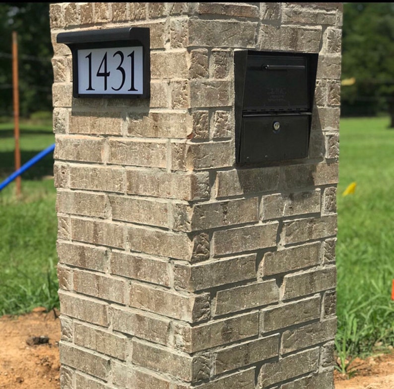 May include: A brick pillar with a black mailbox and address plaque. The address plaque displays the number "1431" in black against a white background. The mailbox is a standard design with a locking door.