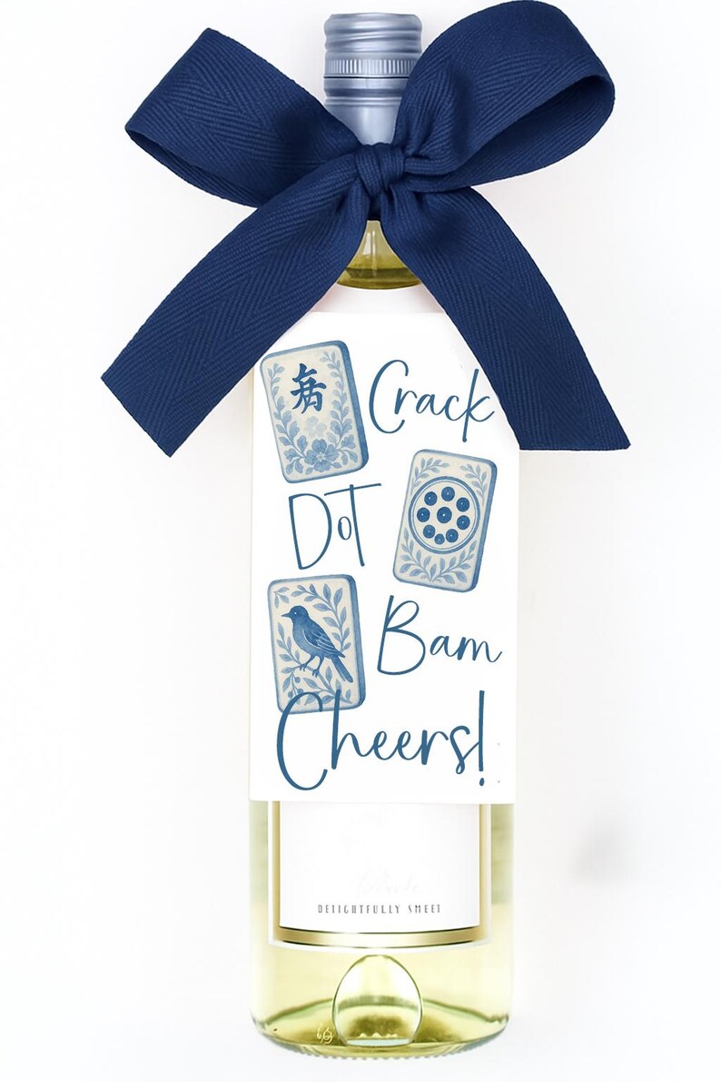 May include: A bottle of white wine with a navy blue bow and a tag featuring Mahjong tile illustrations. The tag reads "Crack Dot Bam Cheers!" in navy blue script. The bottle has a silver cap.