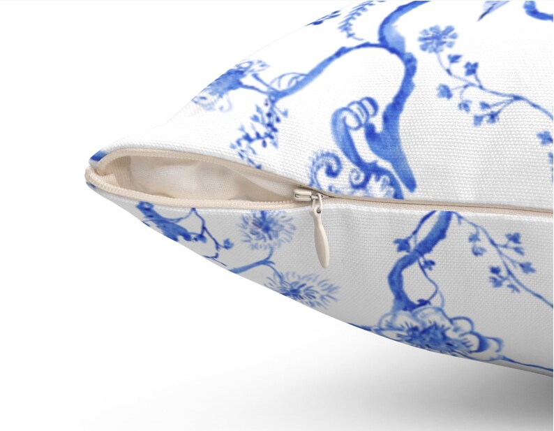 May include: A white pillow with a blue and white floral pattern. The pillow has a zipper closure.