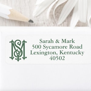 May include: A white return address label with a green monogram of the letters "SM" and the text "Sarah & Mark, 500 Sycamore Road, Lexington, Kentucky 40502".