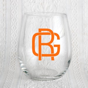 May include: A clear glass wine glass with an orange monogram of the letters "RG" on the front.