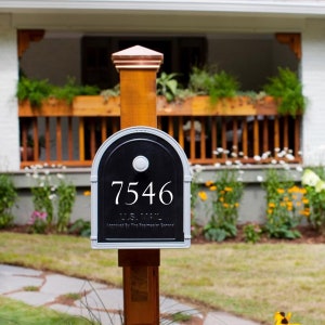 May include: A black mailbox with the number 7546 in white, mounted on a wooden post. The mailbox has a silver trim and a white button. The post is topped with a copper-colored cap. The words "U.S. MAIL" are visible.