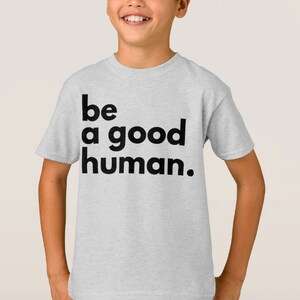 May include: A light grey t-shirt with the text "be a good human." printed in black.