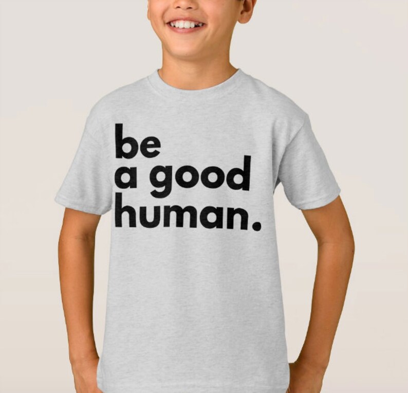 May include: A light grey t-shirt with the text "be a good human." printed in black.