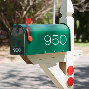 May include: A green mailbox with a white number "950" on the front. The mailbox is mounted on a white wooden post with red accents.